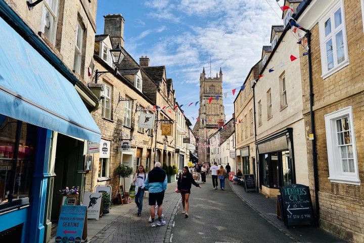 A quaint street with stone buildings, flags, and a distant tower under a blue sky.