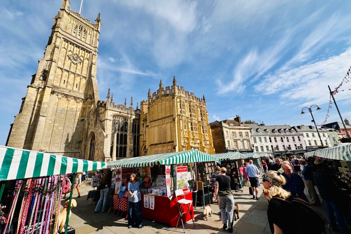 Busy outdoor market with people, stalls, and a historic church under a blue sky.