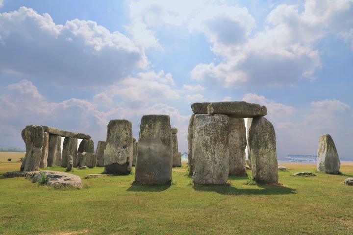 a large stone building with a grassy field with Stonehenge in the background