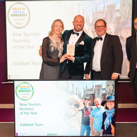 Group of four people in formal attire holding award with 'New Tourism Business of the Year' displayed on screen.