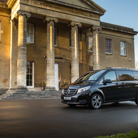 Black Mercedes van parked in front of a large historic building with columns.