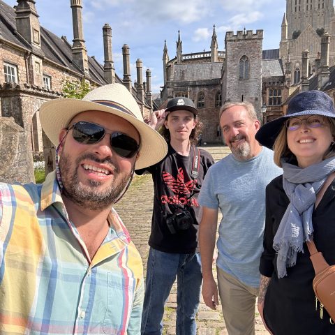 Four people posing in front of historic buildings on a sunny day.