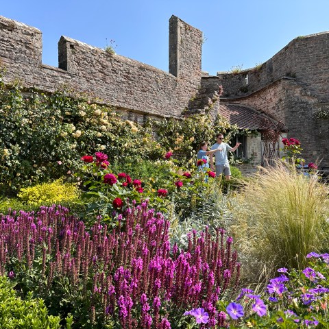 Garden with vibrant flowers and stone walls, two people enjoying the view.