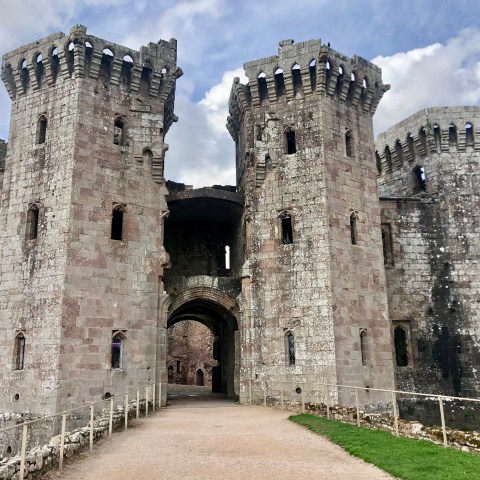 Old stone castle with four large towers and an arched entrance under a cloudy sky.