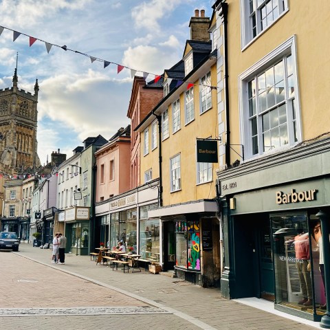 Street with colorful shops, church tower, and bunting overhead on a sunny day.
