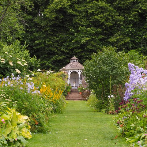 Garden path lined with colorful flowers leading to a white gazebo.
