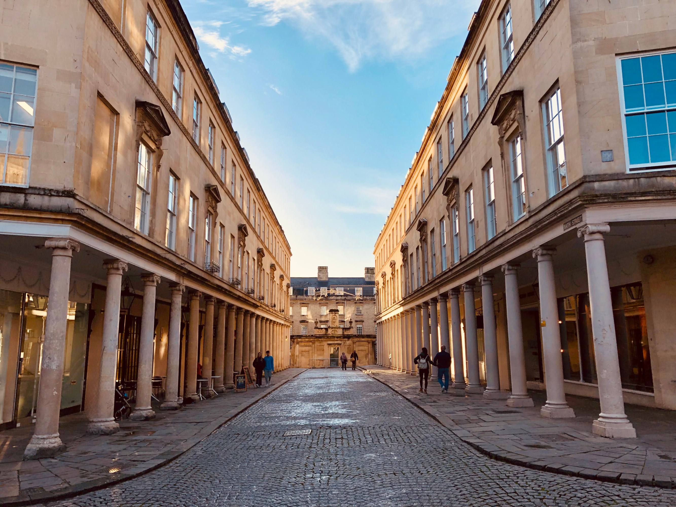 Cobblestone street between neoclassical buildings under a clear sky.