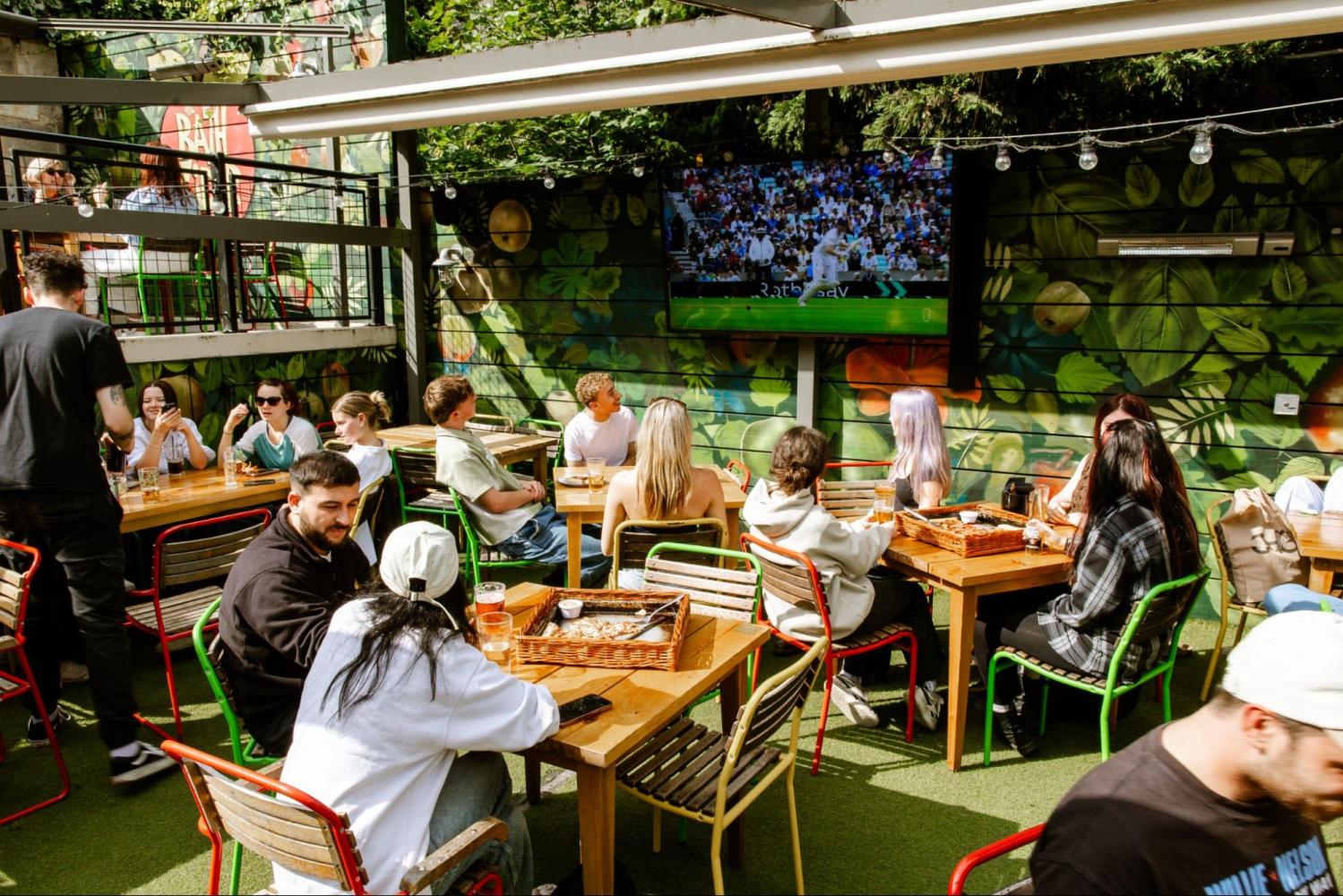 People sitting outdoors watching sports on TV at a cafe.