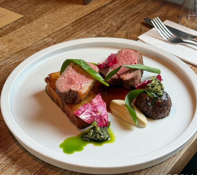 Gourmet plated meal with meat, greens, sauce, and garnishes on white dish.