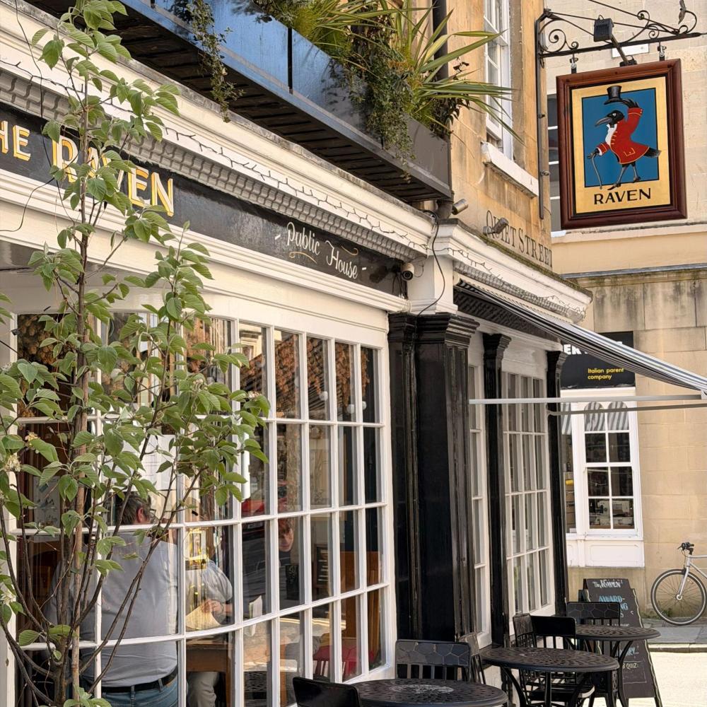 Outdoor seating at a pub named Raven with plant decor and hanging sign.