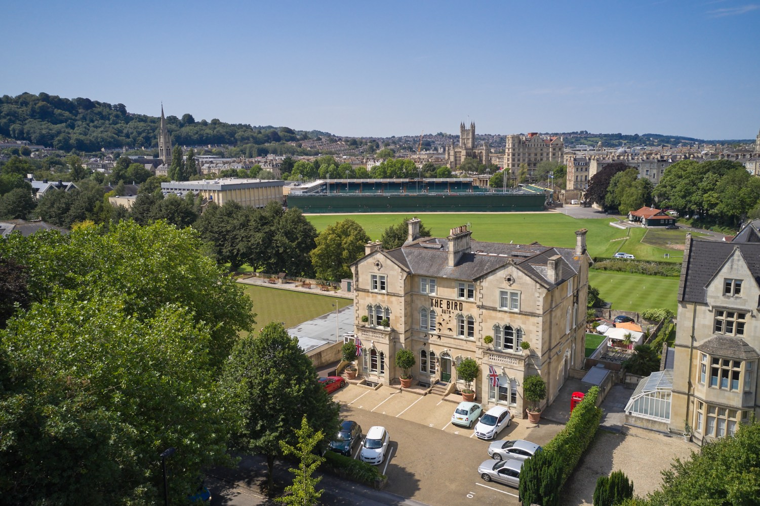 Aerial view of a historic building and a cricket field in Bath, UK.
