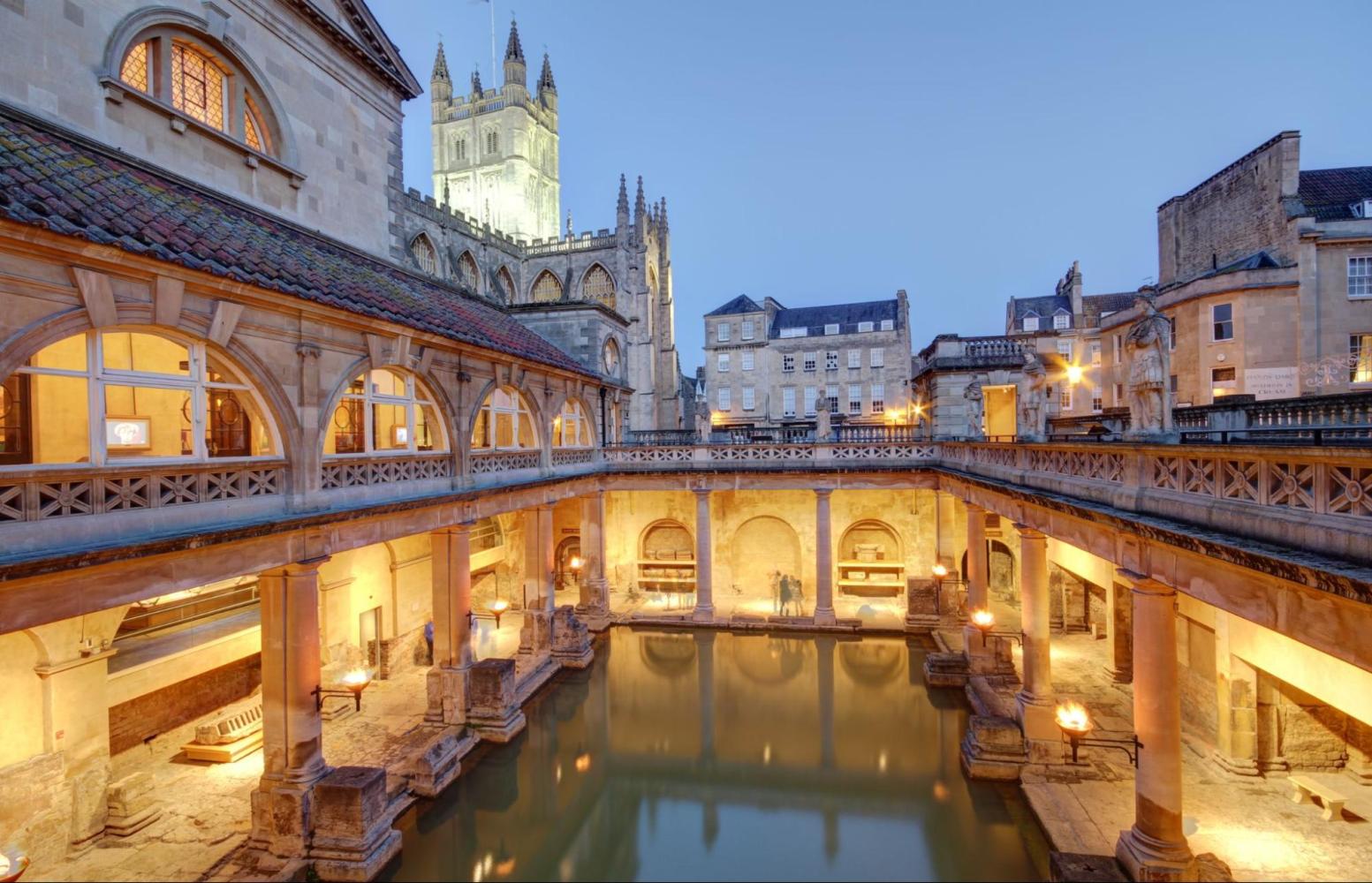 Roman-style bath with illuminated arches and a cathedral in the background.