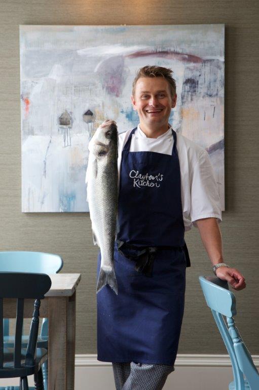 Person in apron holding a large fish, standing in a kitchen.